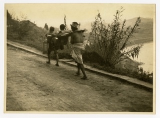 Image: photograph: two men carrying person in chair